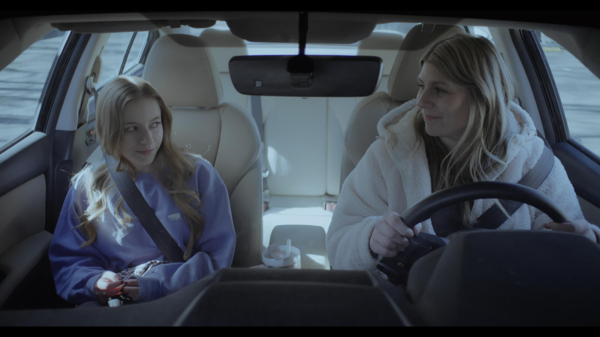 The protagonist and her daughter share a happy look, sitting in their car, illuminated by the light of the morning.