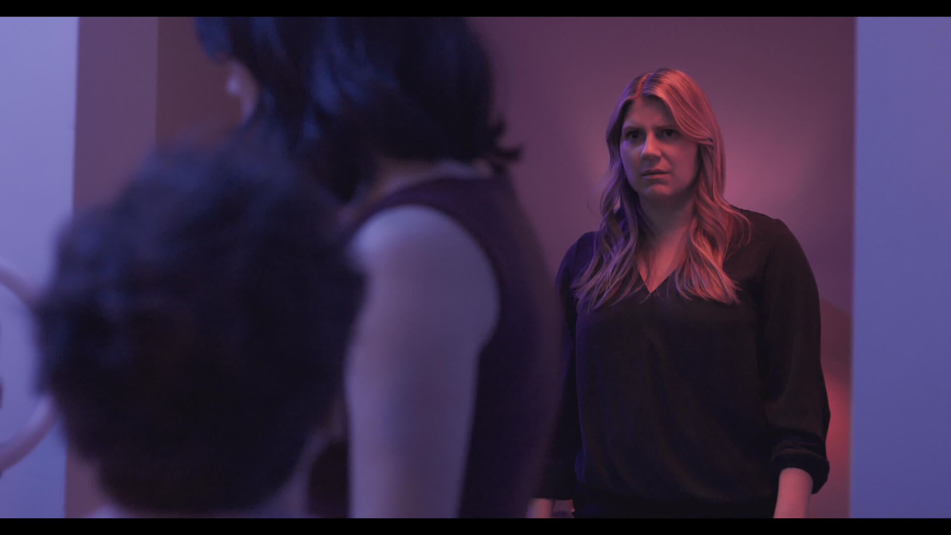 Method and Madness Still 3 The protagonist of Method and Madness standing in a doorframe with colored lighting. She looks horrified at the antagonist and his associate.