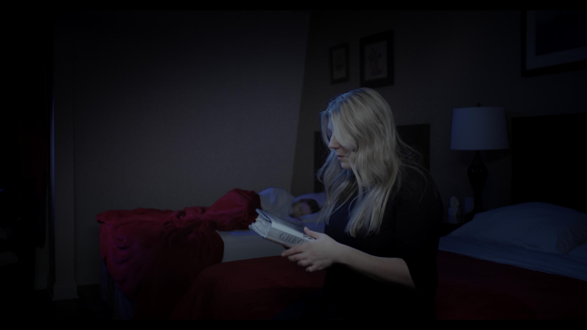 The lead of Method and Madness sits on the edge of her bed, looking contemplatively at a book.