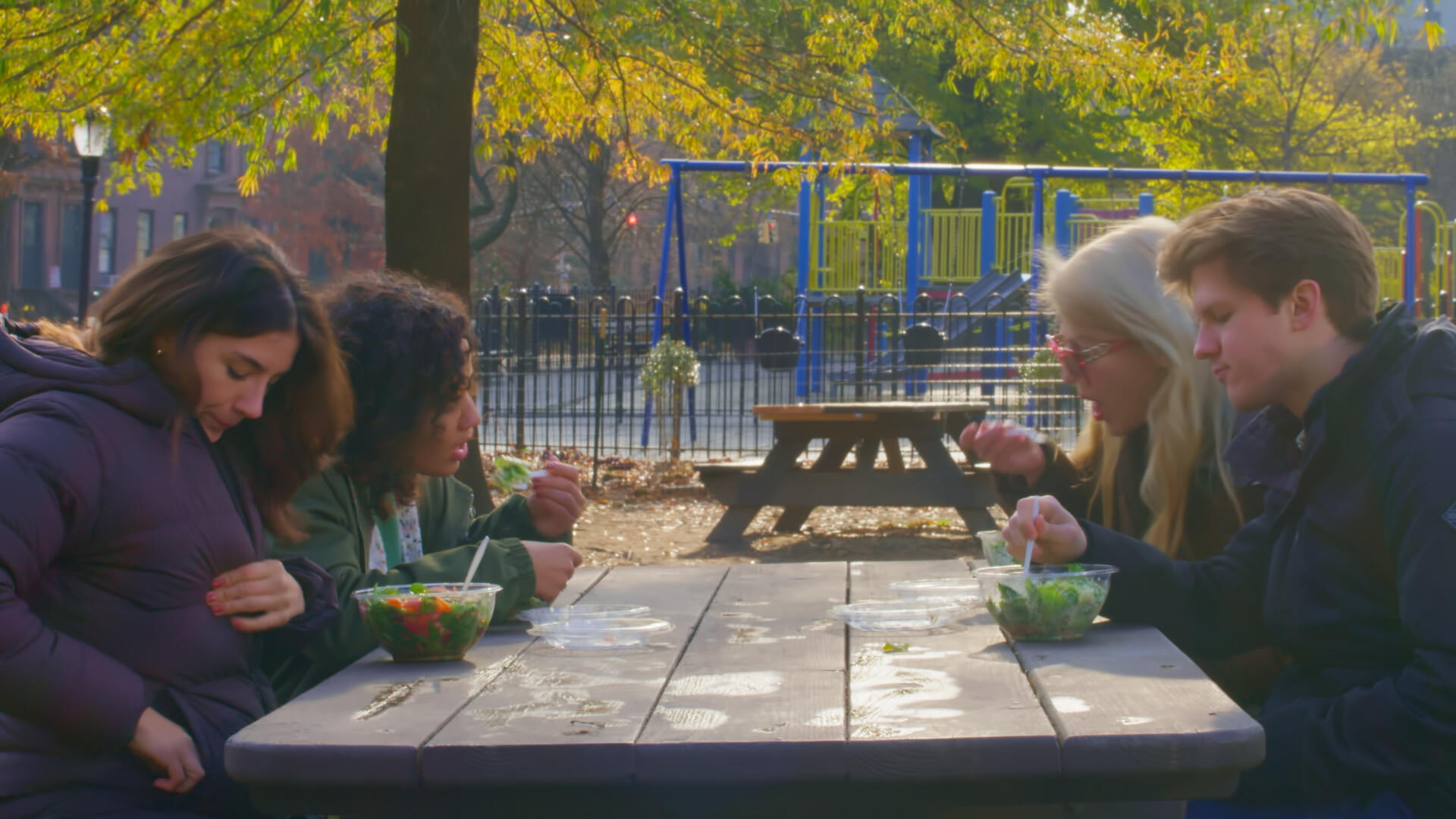 Late Bloomers Still 2 Four leads of Late Bloomers sit in a park at a picnic table, all eating salads.