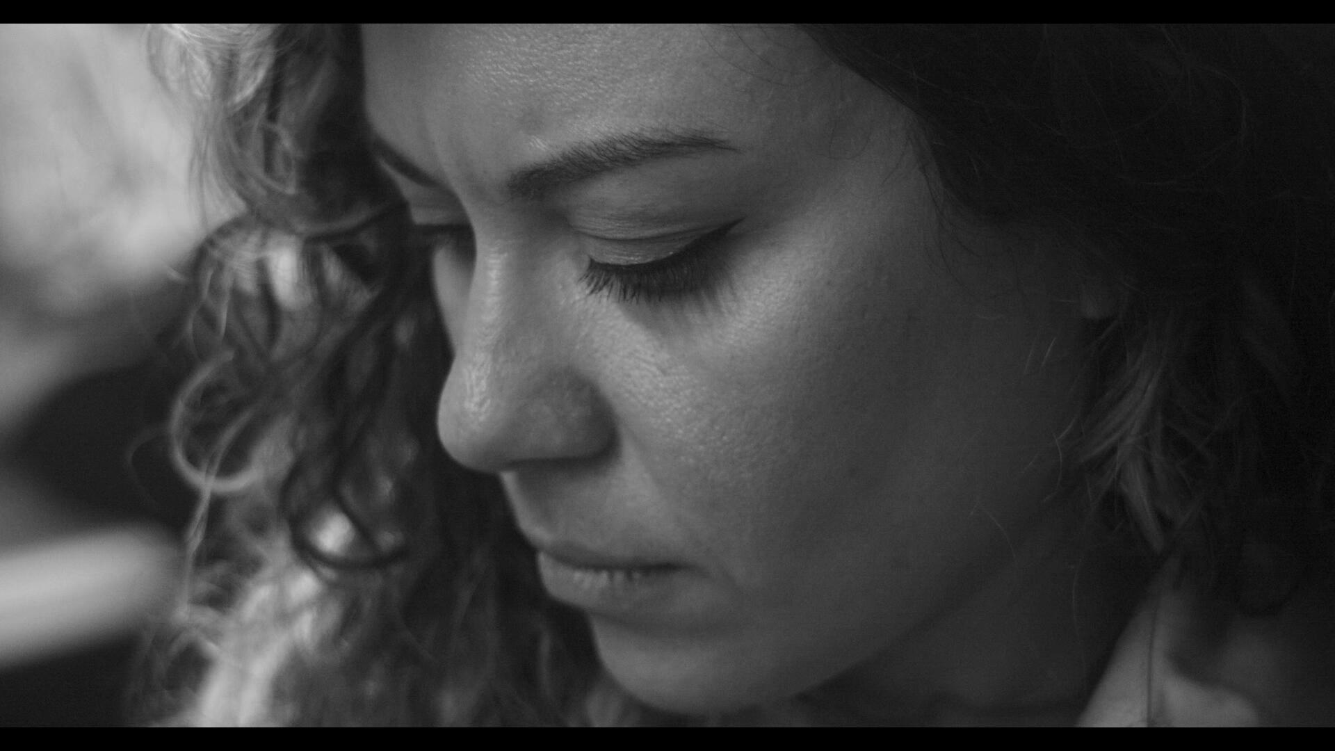 A closeup of Patricia, sitting, looking down, and thinking deeply.